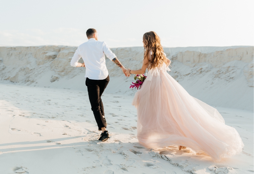 結婚するカップルが砂浜を歩く写真